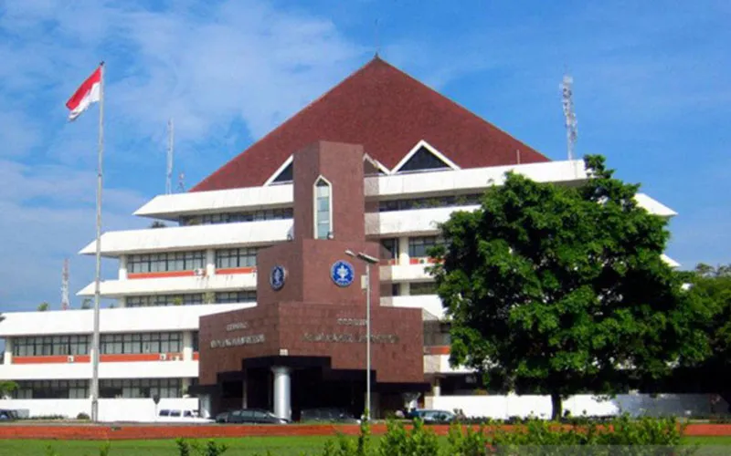 Gedung Rektorat IPB University yang megah dengan mahasiswa berjalan di depannya, dikelilingi oleh taman hijau yang asri dan beberapa bangunan akademik lainnya.