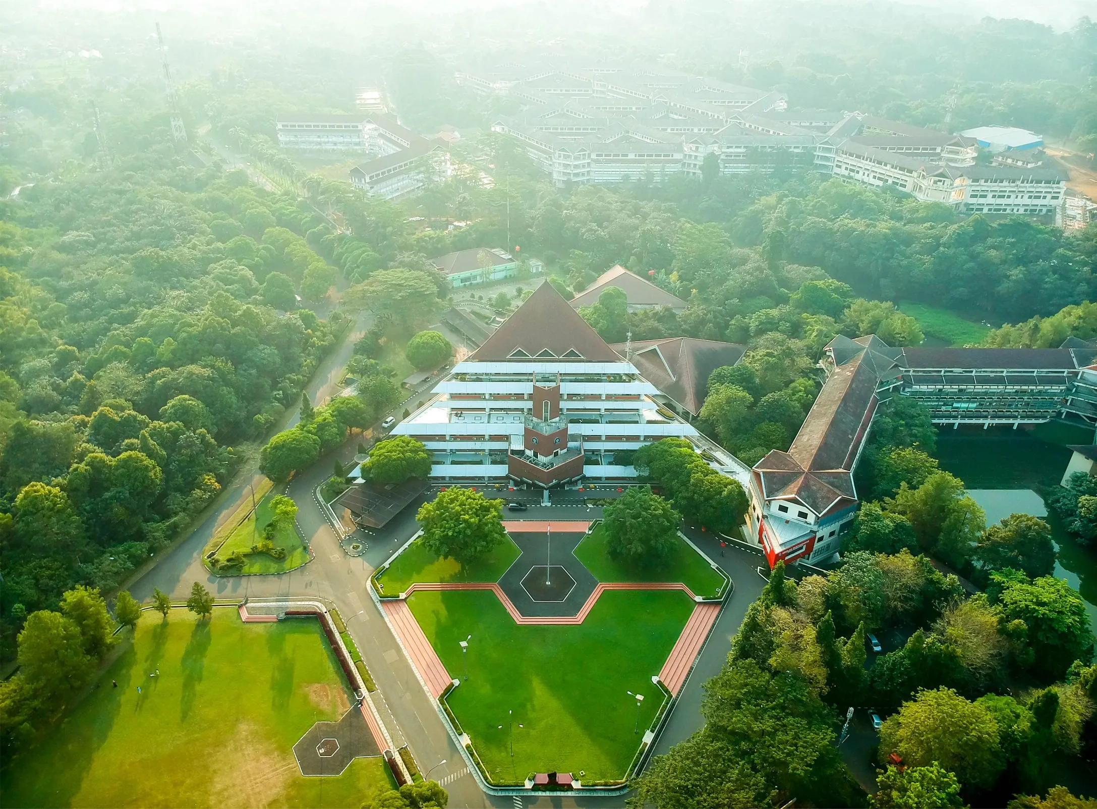 Gedung rektorat IPB yang megah dikelilingi oleh area hijau yang luas, dengan mahasiswa berjalan di trotoar.